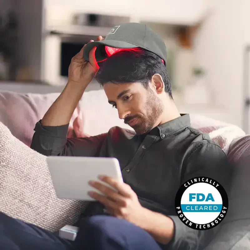 Man using hair growth laser cap while reading on a tablet, showcasing the PowerFlex model for hair regrowth.