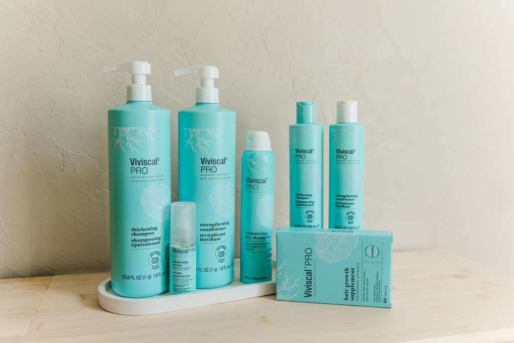 Viviscal Pro thickening conditioner and other hair care products displayed on a wooden shelf.