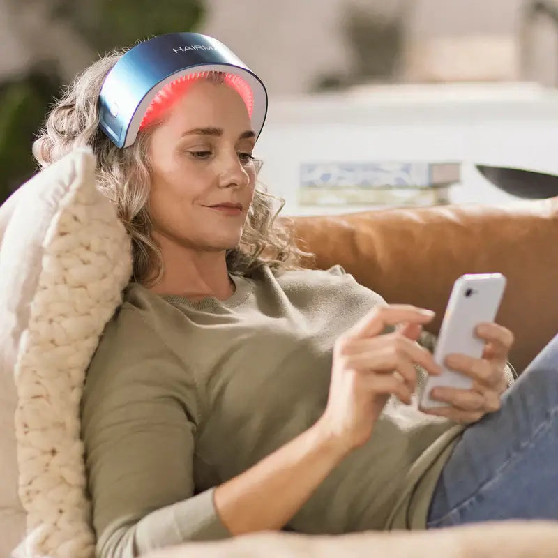 Woman using LaserBand 82 hair growth device while relaxing on a couch.