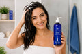 Woman holding Pharma Hermetic Anti Hair Loss Shampoo Blue Line in bathroom, showcasing healthy hair care.